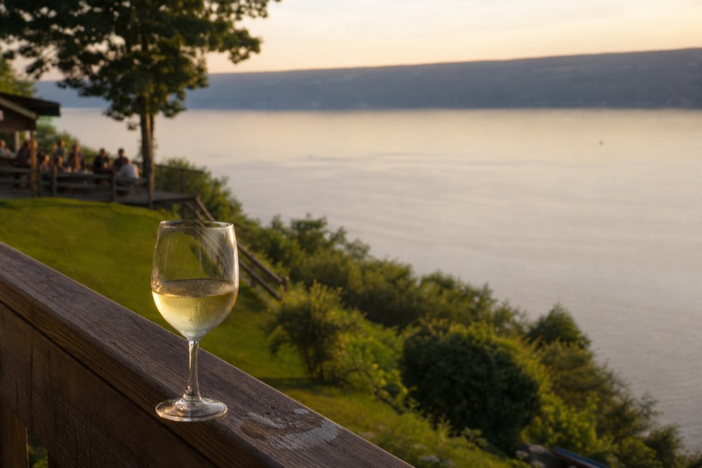 A glass of white wine on a winery deck overlooking Seneca Lake, no text, no logos, no people
