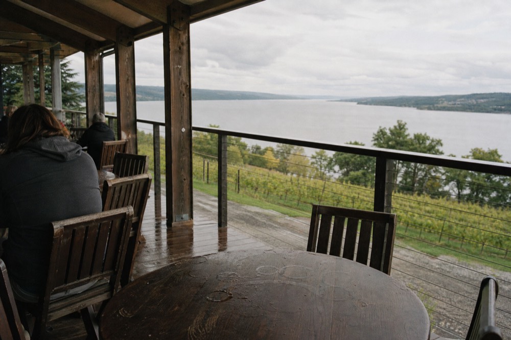 A tasting room patio overlooking Seneca Lake with vineyard slopes beyond, no text, no logos, no people