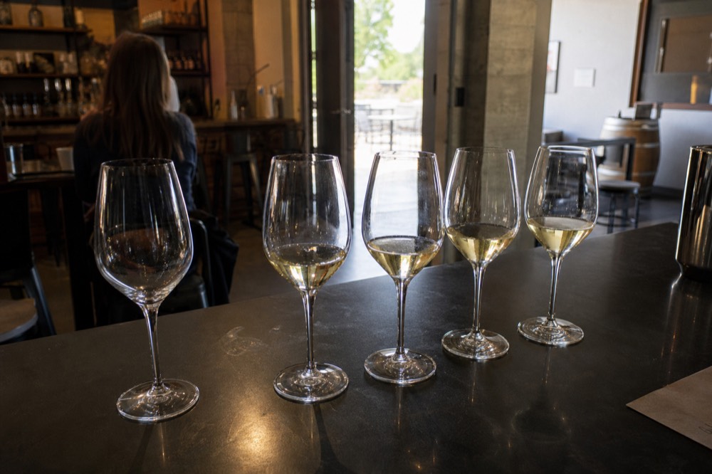 A tasting flight of white wines on a winery tasting bar, no text, no logos, no people