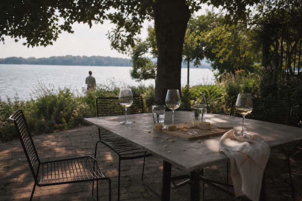 A lakeside lunch table with glasses of white wine and a cheese board, no text, no logos, no people