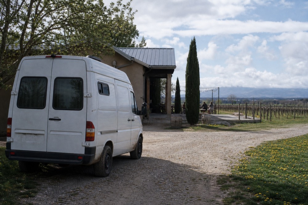 A small touring van parked beside a vineyard tasting room, no text, no logos, no people