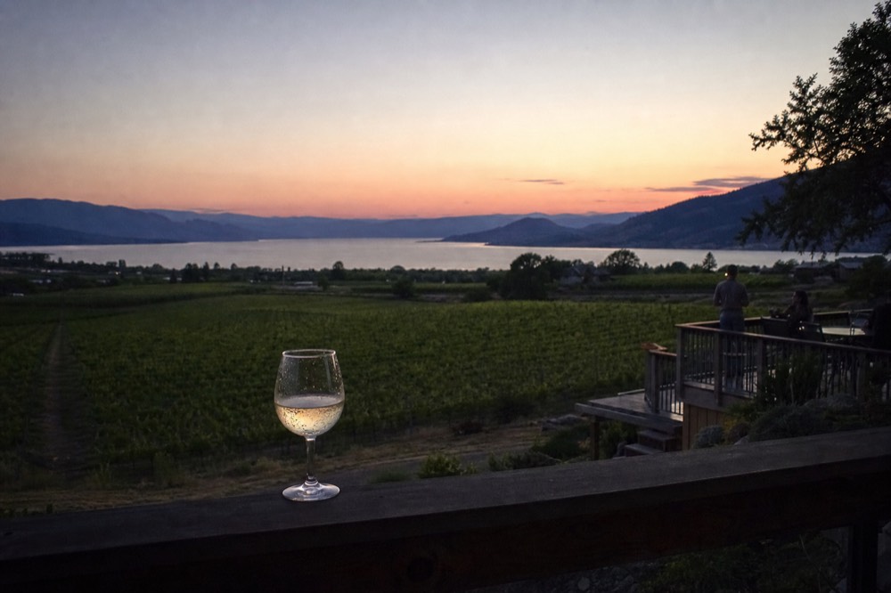 A lakeside lodging balcony overlooking vineyards and water at dusk, no text, no logos, no people