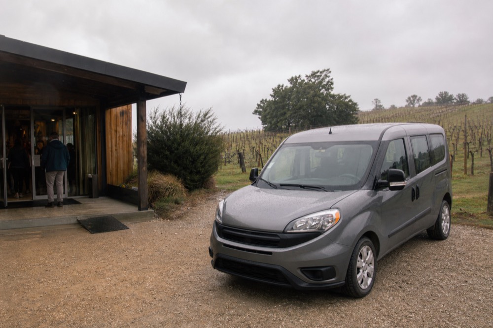 A small van parked outside a Finger Lakes tasting room with vines behind it, no text, no logos, no people