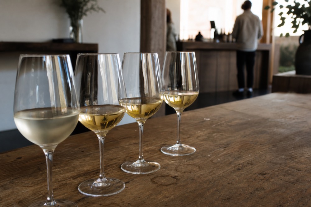 A tasting flight of white wines on a wooden tasting room counter, no text, no logos, no people