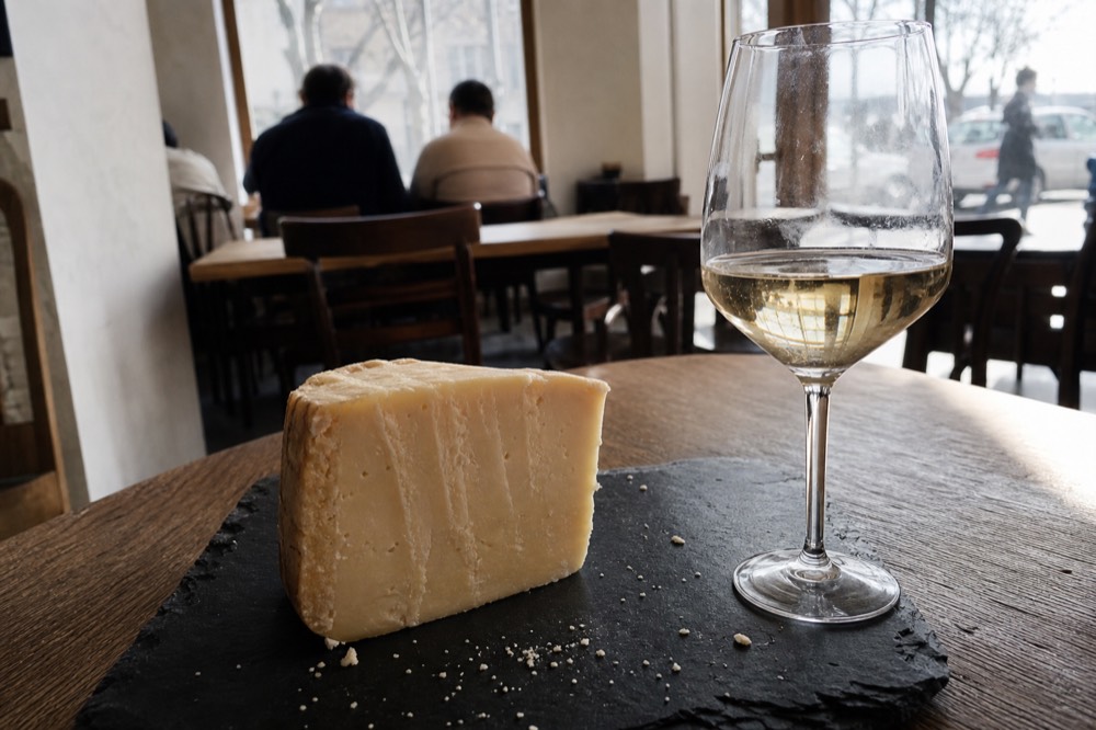 A wedge of aged cheese and a glass of white wine on a slate board, no text, no logos, no people