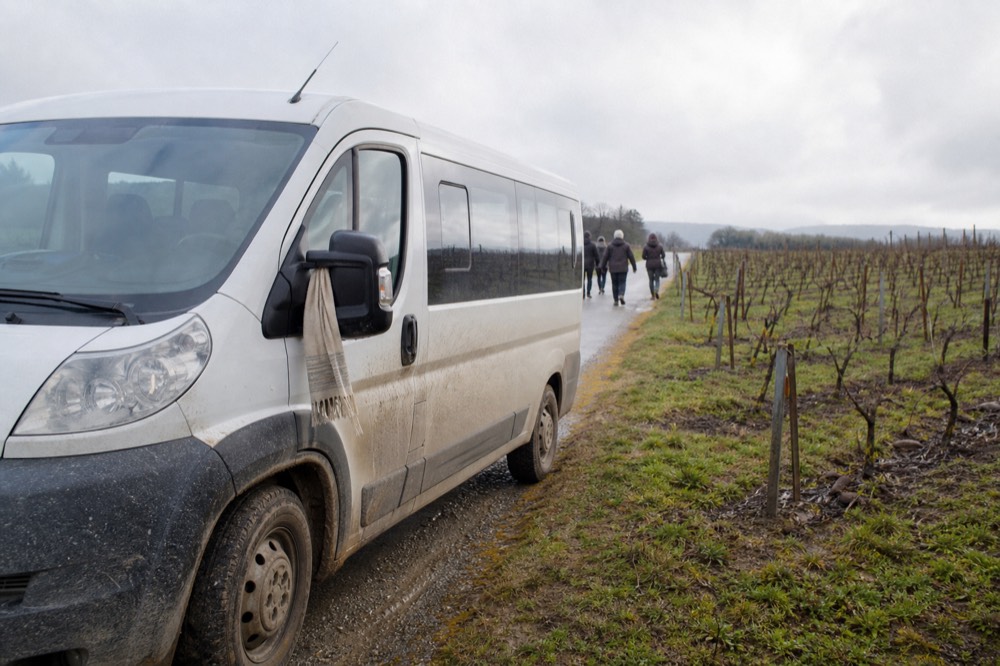A small tour van parked on a rural road beside rows of vineyards, no text, no logos, no people