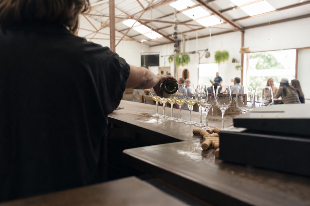 A guide pouring wine for glasses arranged along a tasting room bar, no text, no logos, no people