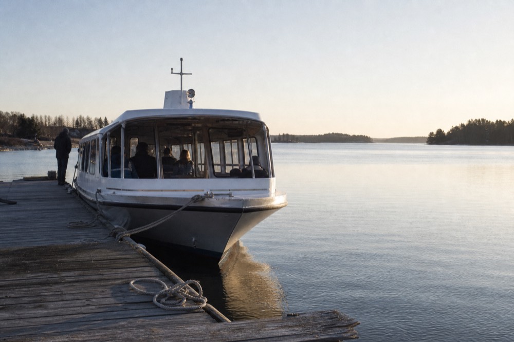 A small passenger cruise boat moored at a wooden dock on a lakefront, morning light on the water, no text, no logos, no people
