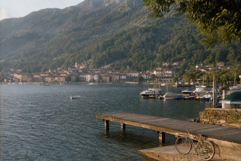 A small lake town seen across calm water, boats at docks, hills behind, no text, no logos, no people