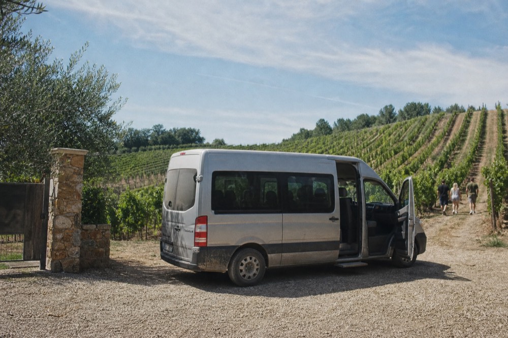 A small van parked at a winery entrance with vineyards behind, no text, no logos, no people