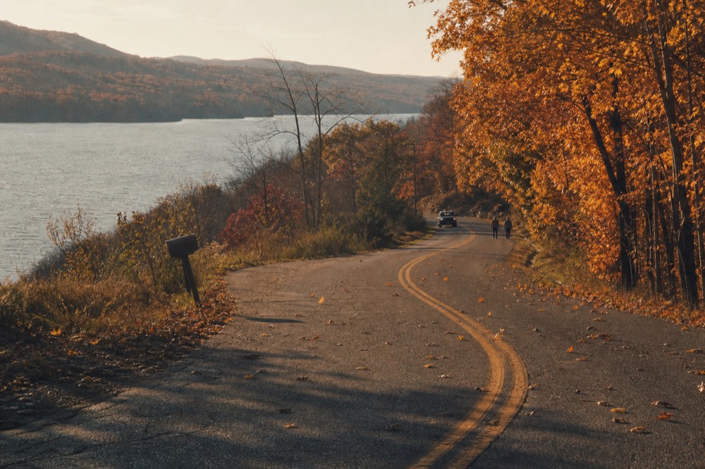 Rural two-lane road curving along a hillside above a Finger Lake, no text, no logos, no people