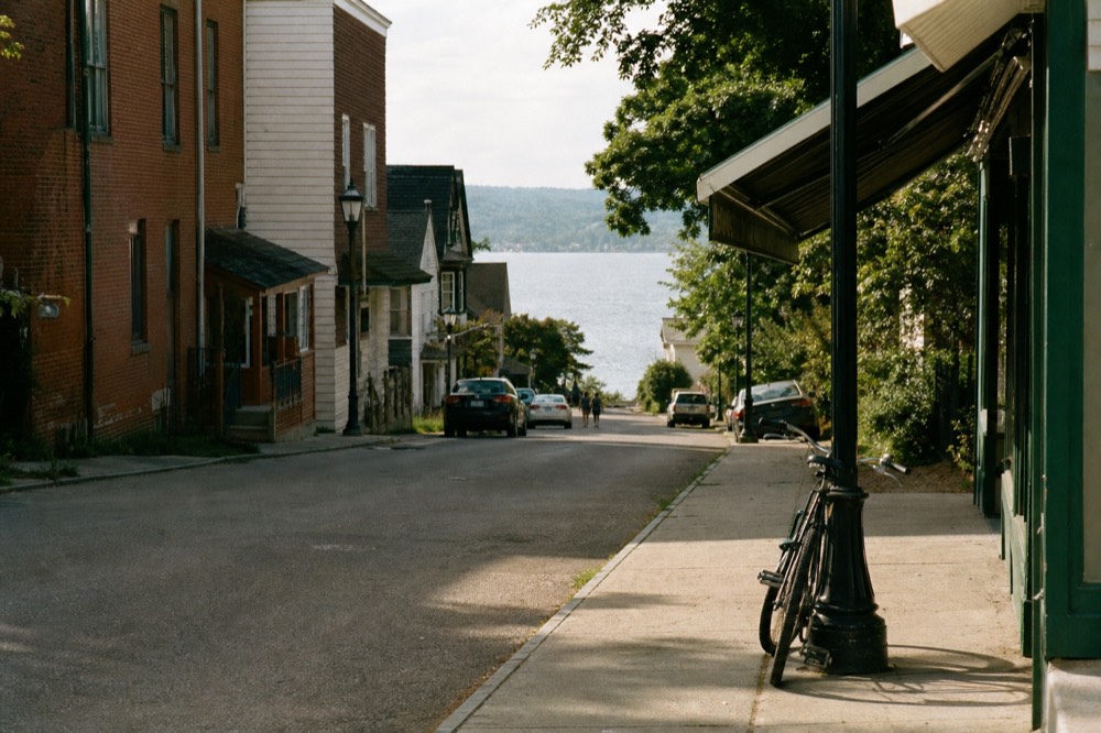 Small-town main street with a village park and lake beyond the rooftops, no text, no logos, no people