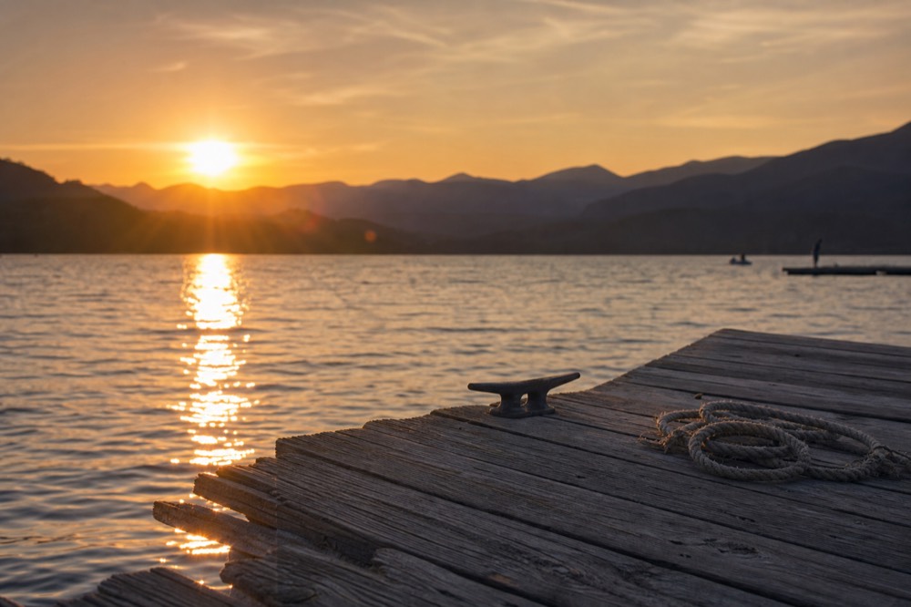 Lakeside dock at sunset with calm water and hills behind, no text, no logos, no people