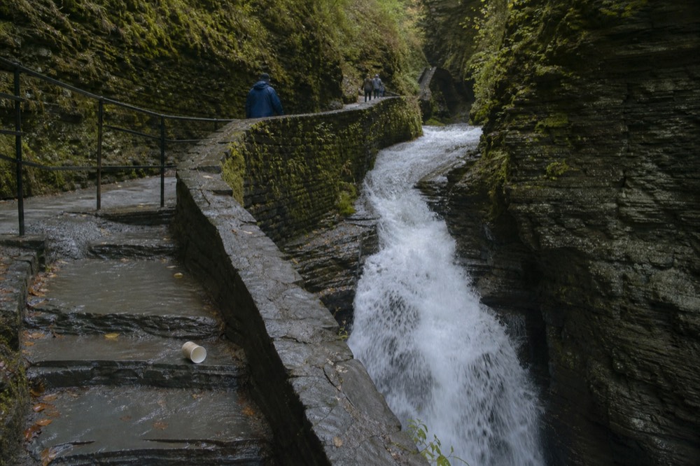 Waterfall dropping through a rock gorge with a stone staircase alongside, no text, no logos, no people