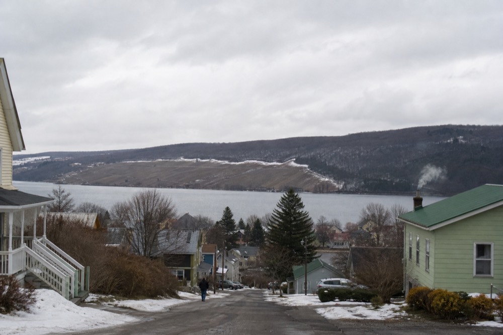 A village at the south tip of a Finger Lake with hills and vineyards behind, no text, no logos, no people